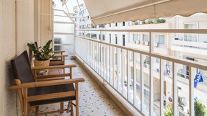 Un balcó amb vista a un paisatge urbà, una planta en test i una cadira de fusta.