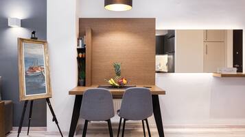 A modern dining area with a wooden table, two grey chairs, a painting on easels, and a fruit bowl.