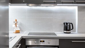 Una cuina moderna amb electrodomèstics d'acer inoxidable, com ara una placa de cocció, forn i cafetera a la tauleta.