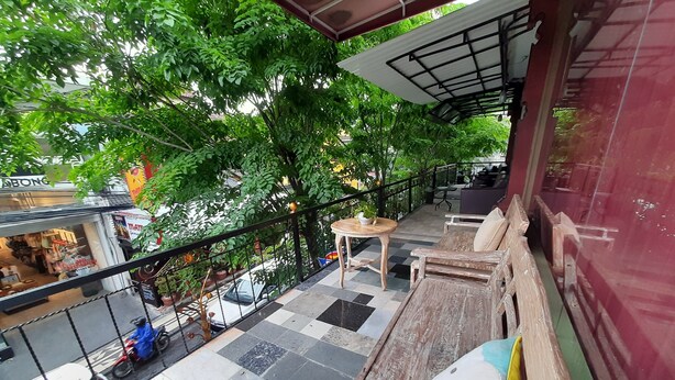 Een balkon met een geruite vloer, houten meubels en uitzicht op een straat met winkels en bomen.