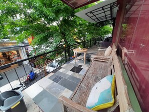 A balcony with a checkered floor, wooden furniture, and a view of a street with shops and trees. - The Legian 777 Guest House (Legian)