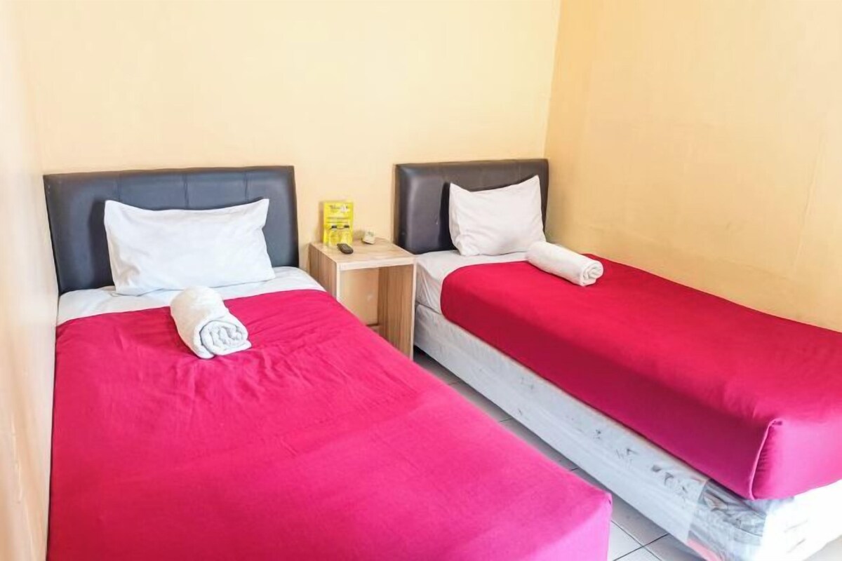 Two single beds with red bedding, a wooden nightstand, and a yellow object on the nightstand.