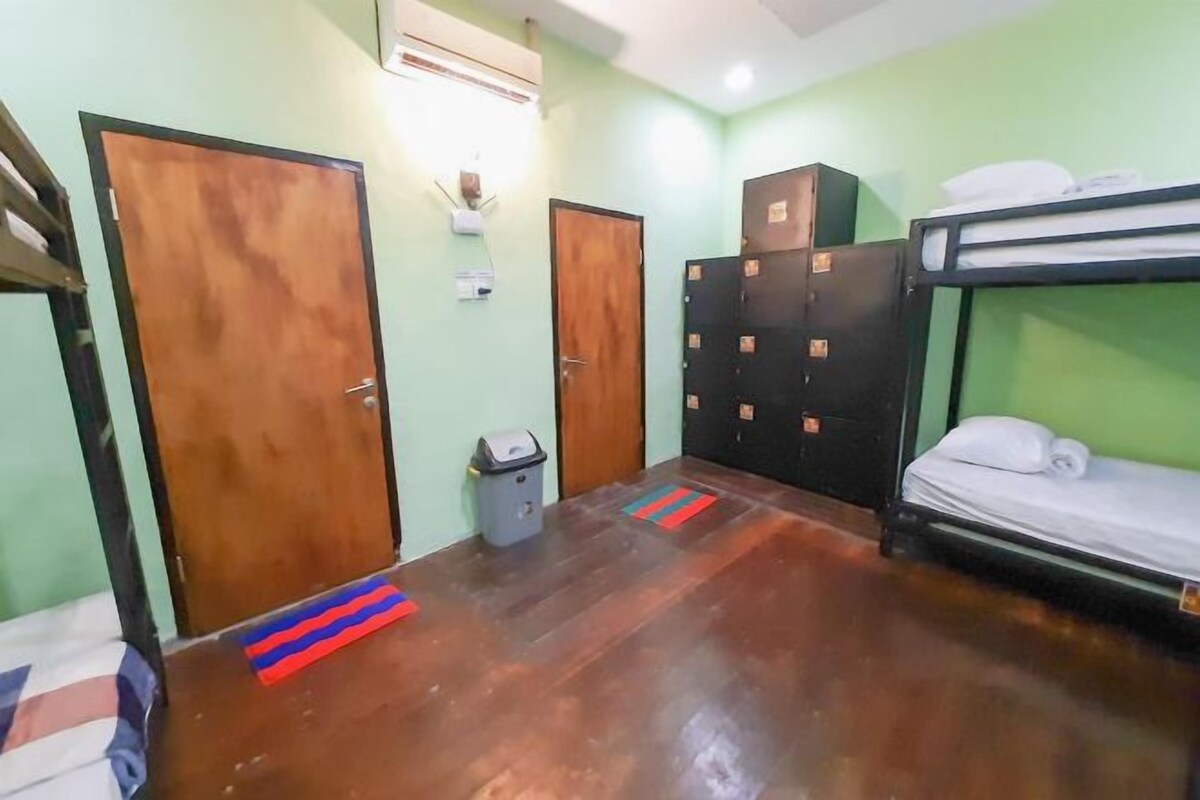 A room with bunk beds, a wooden floor, a trash bin, and a wall-mounted air conditioner.