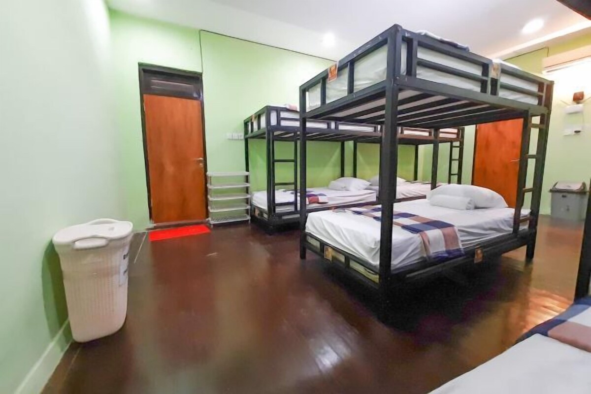 Une chambre avec des lits superposés, un plancher en bois, une poubelle blanche et une porte visible au fond.