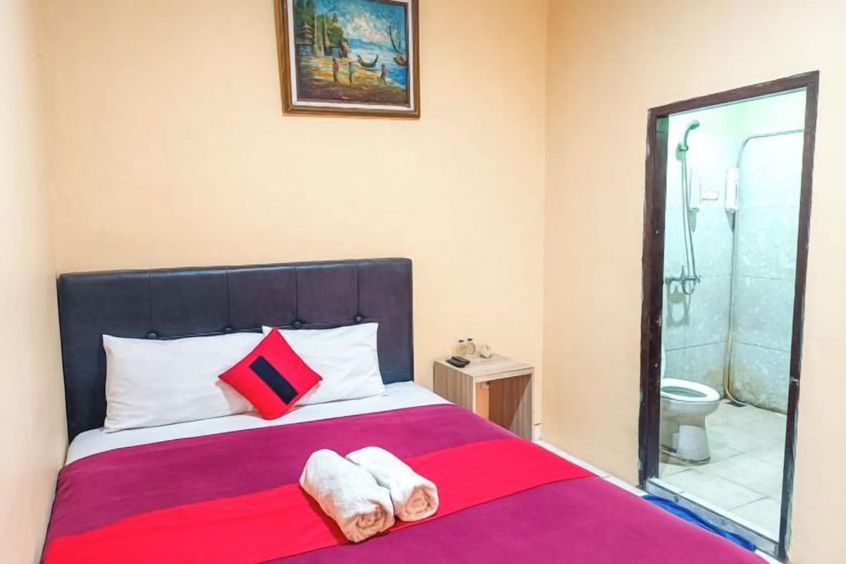 Een hotelkamer met een bed, een schilderij aan de muur en een badkamer door een geopende deur.