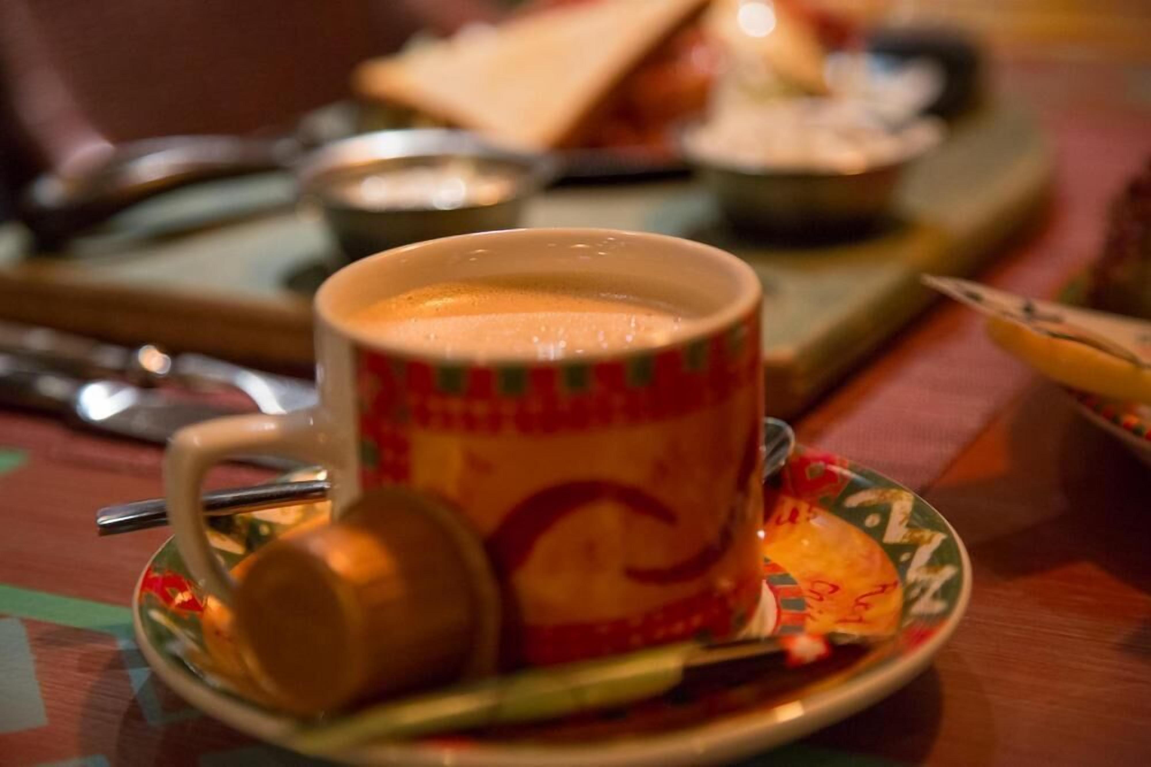 Eine Kaffeetasse auf einem Untertasse mit einem Löffel, ein Teller mit Gebäck und eine kleine Schale auf einem Tisch.