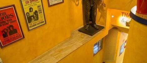 Una estatua de un hombre trajeado sobre un pedestal en una habitación con paredes amarillas, carteles en la pared y una escalera.