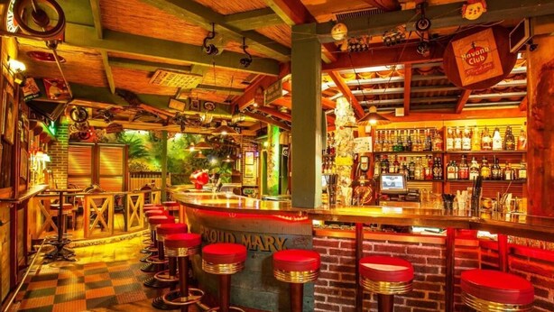 A bar with a wooden ceiling, a counter with stools, and shelves of bottles. - Hotel California (Zürich)