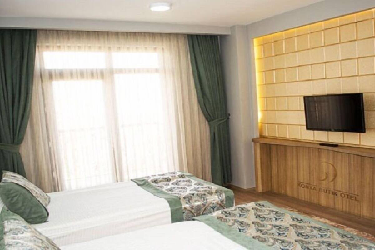 A hotel room with two beds, a TV mounted on a wooden panel wall, and a large window with curtains.