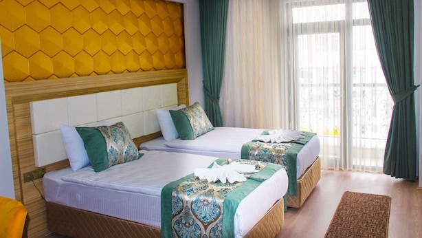Een hotelkamer met twee bedden, een houten hoofdbord, groene gordijnen en uitzicht.