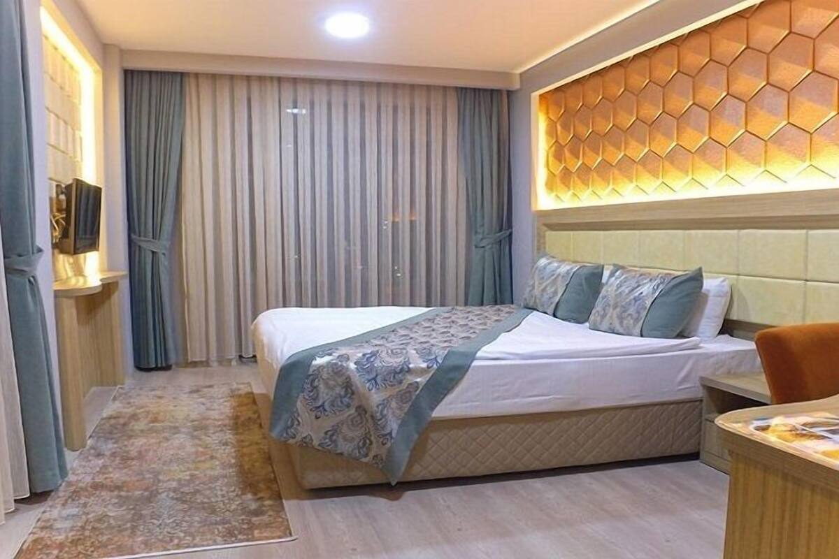 A hotel room with a large bed, a wooden headboard, a small desk, and a television on a stand.