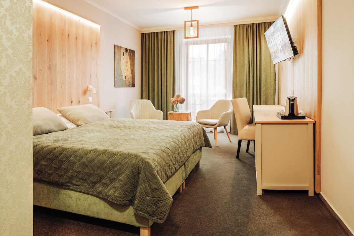 A hotel room with a bed, a desk, a chair, a TV, and a window with curtains.