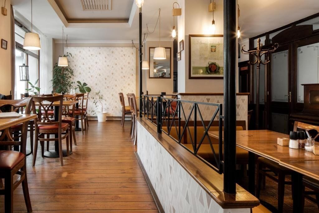 Interior de restaurante con suelo de madera, mesas, sillas e iluminación colgante.