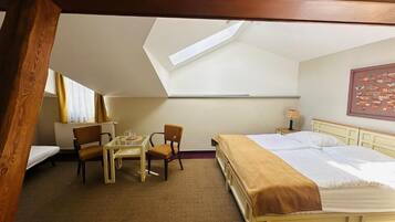 A room with a bed, a table, two chairs, a radiator, and a skylight.
