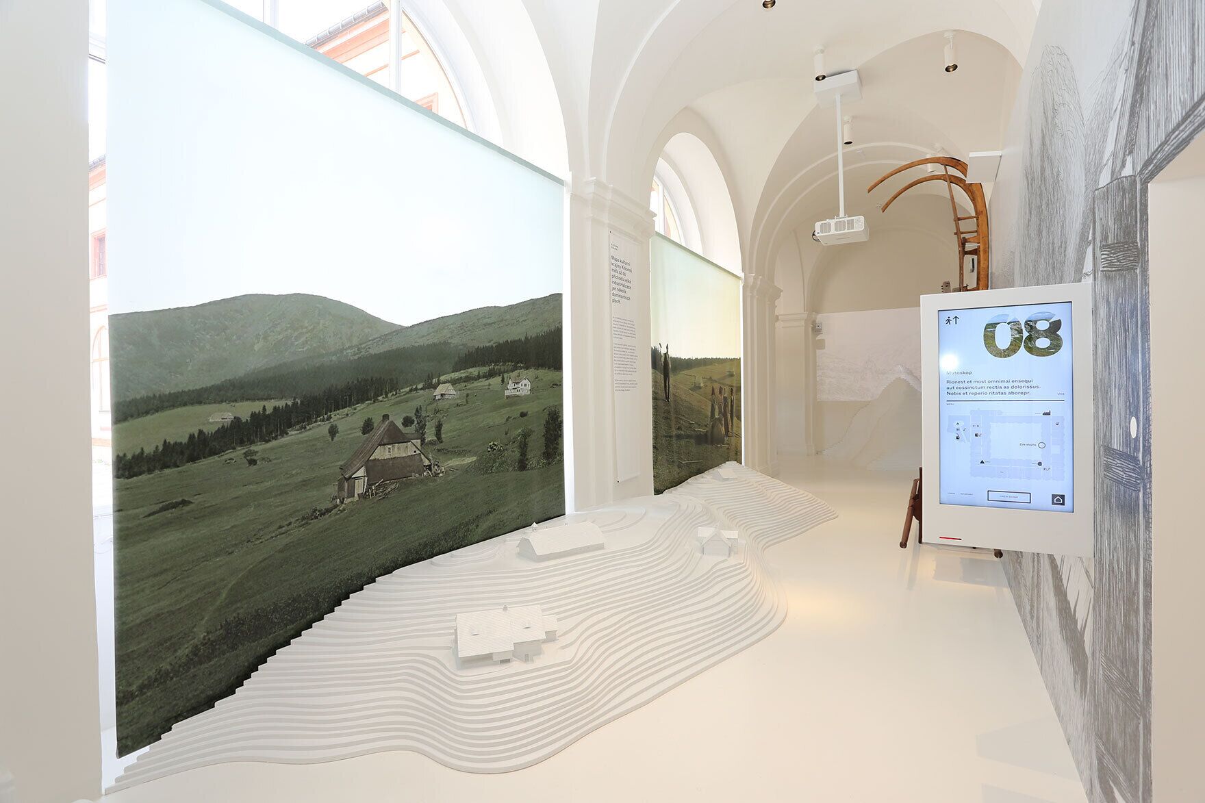 A gallery with a large landscape painting, a digital display, and a unique floor design.