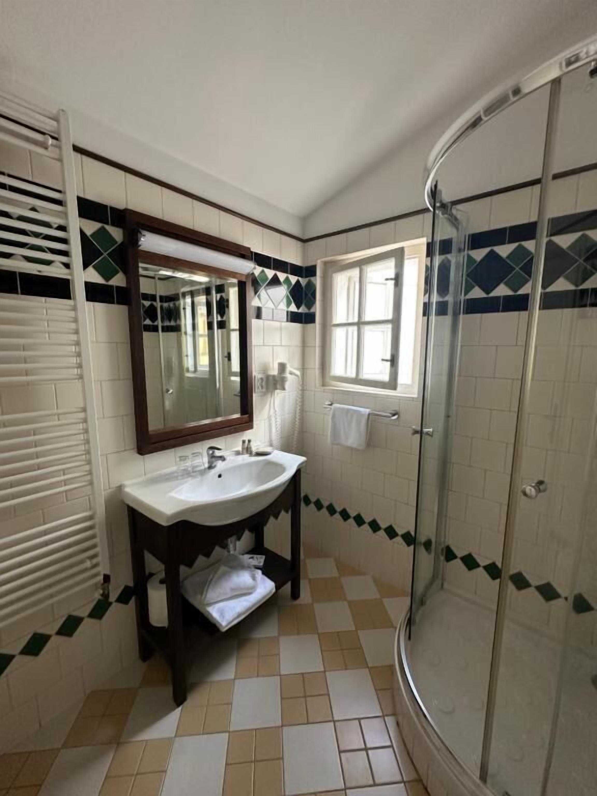 A bathroom with a sink, mirror, window, and shower.