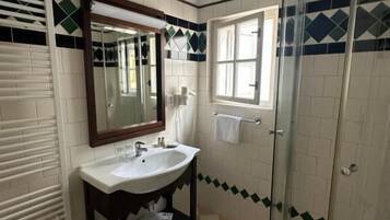 A bathroom with a sink, mirror, window, and shower.