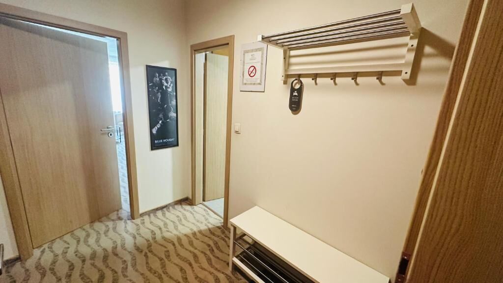 Un pasillo con alfombra estampada, una puerta, un cartel, una señal de no fumar y un calentador fijado a la pared.