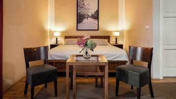 A hotel room with a bed, two nightstands, a bedside table with a vase of flowers, two chairs, and a framed picture on the wall.