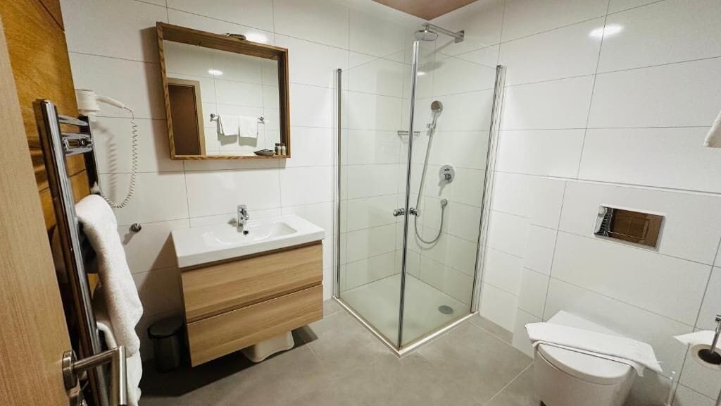 Une salle de bain moderne avec une douche à parois de verre, un meuble-lavabo en bois et un lavabo blanc.