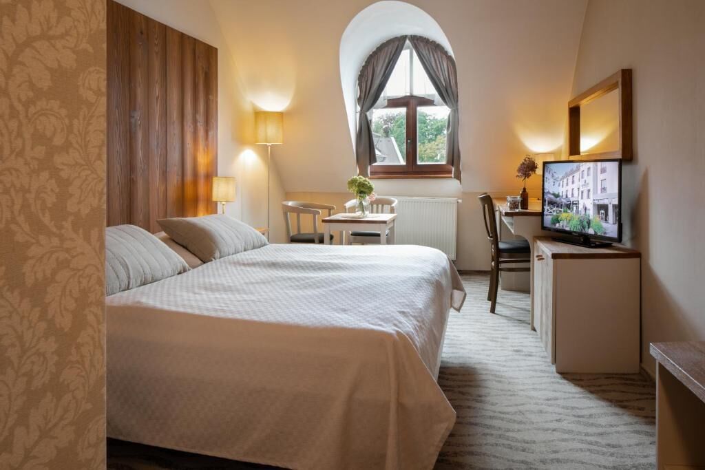 A hotel room with a bed, a desk, a chair, a television, and a window with curtains.