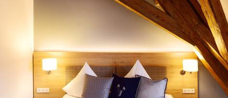 Un dormitorio con techo de madera, una cama con ropa de cama blanca y dos almohadas, y dos lámparas fijadas a la pared.
