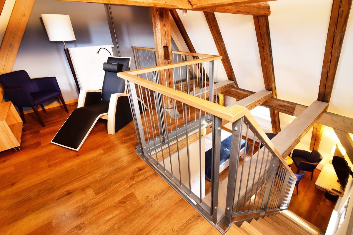 A loft-style room with a wooden staircase, a desk, a chair, and a lamp.
