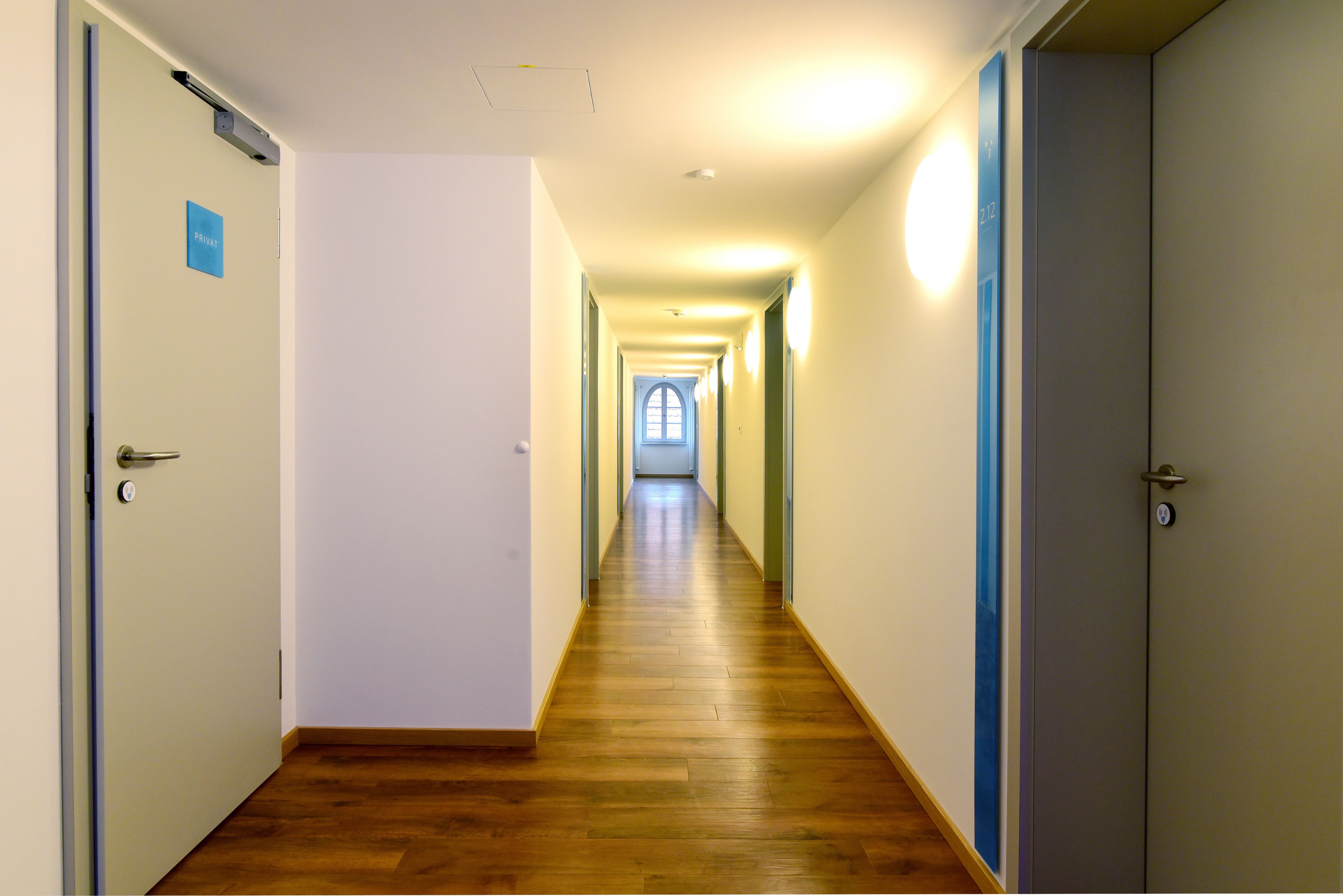 A long, narrow hallway with wooden flooring and doors on both sides.