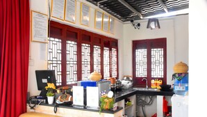 A kitchen with a brick counter, a sink, and a water dispenser. There are windows with decorative grills, a red curtain, and a computer on the counter. - Shi Lin family folk inn (Kunming)