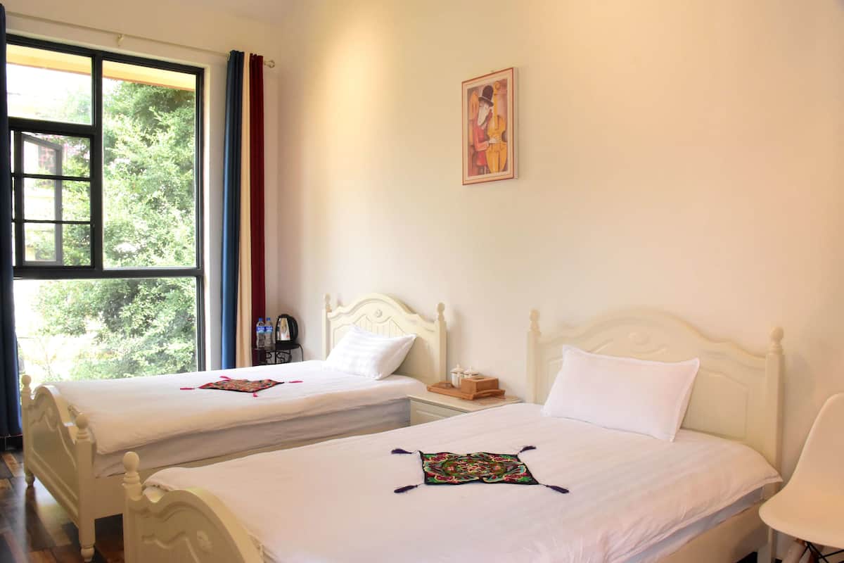 Habitación de hotel con dos camas, una ventana con cortinas, un cuadro en la pared y una silla.