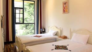 A hotel room with two single beds, a window with curtains, a bedside table with a lamp, and a painting on the wall. - Shi Lin family folk inn (Kunming)