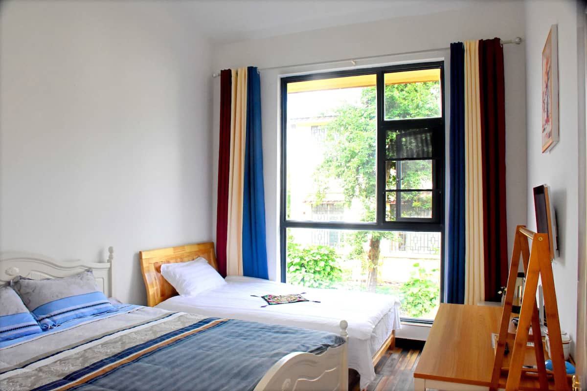 Un dormitorio con dos camas, una ventana con cortinas y un caballete de madera.
