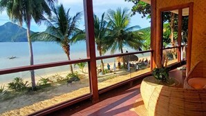 Ein Zimmer mit großem Fenster und Meerblick, ein Korbstuhl und ein kleiner Tisch.