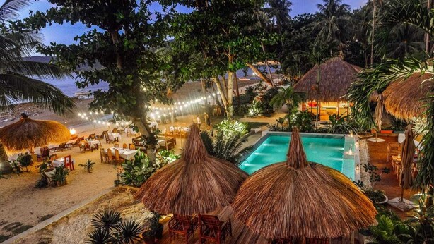 Ein Resort mit strohgedeckten Gebäuden, einem Pool und mehreren Essbereichen im Freien.