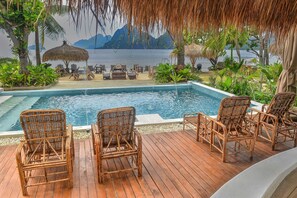 A poolside area with wicker chairs and a view of a mountain range.