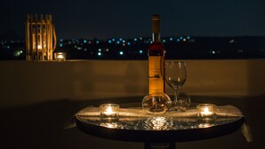 A table with a bottle of wine, a glass, and candles on a balcony with a cityscape and moon in the background. - Villa Iasmi (Chania)