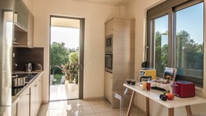 A modern kitchen with a dining area, a large window, and a view of greenery outside. - Villa Iasmi (Chania)