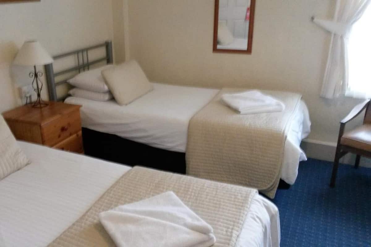 A hotel room with two beds, a nightstand, a lamp, and a chair.
