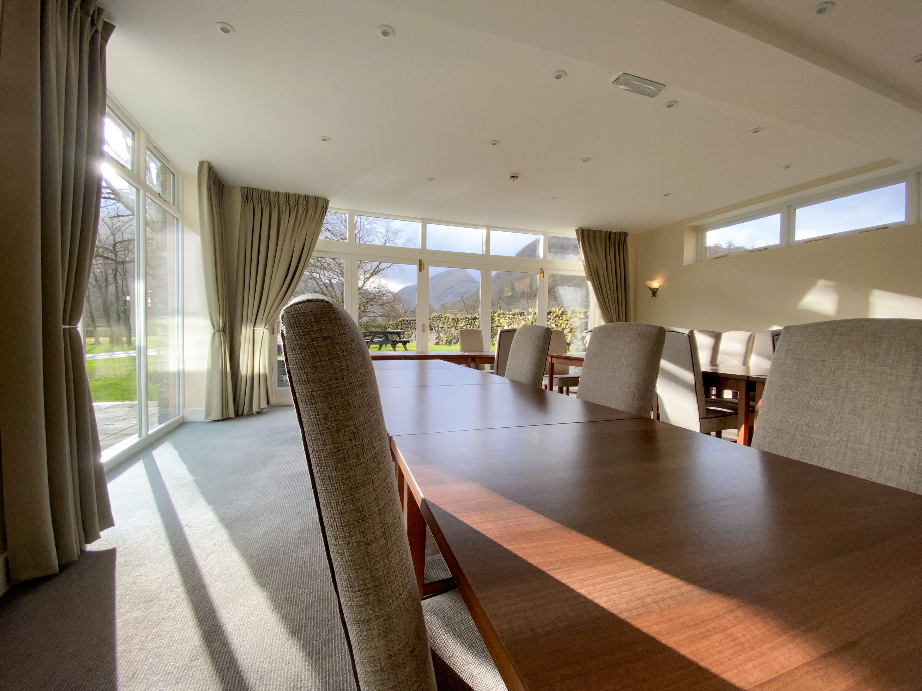 A conference room with a long table and chairs, large windows with curtains, and a view of the outdoors.