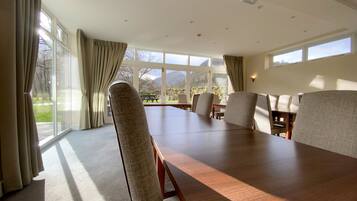 A conference room with a long table and chairs, large windows with curtains, and a view of the outdoors.