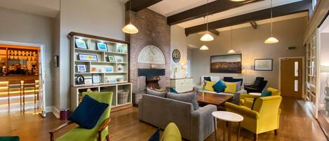 A spacious lobby with a fireplace, a bar area, and a seating area with green and yellow chairs.