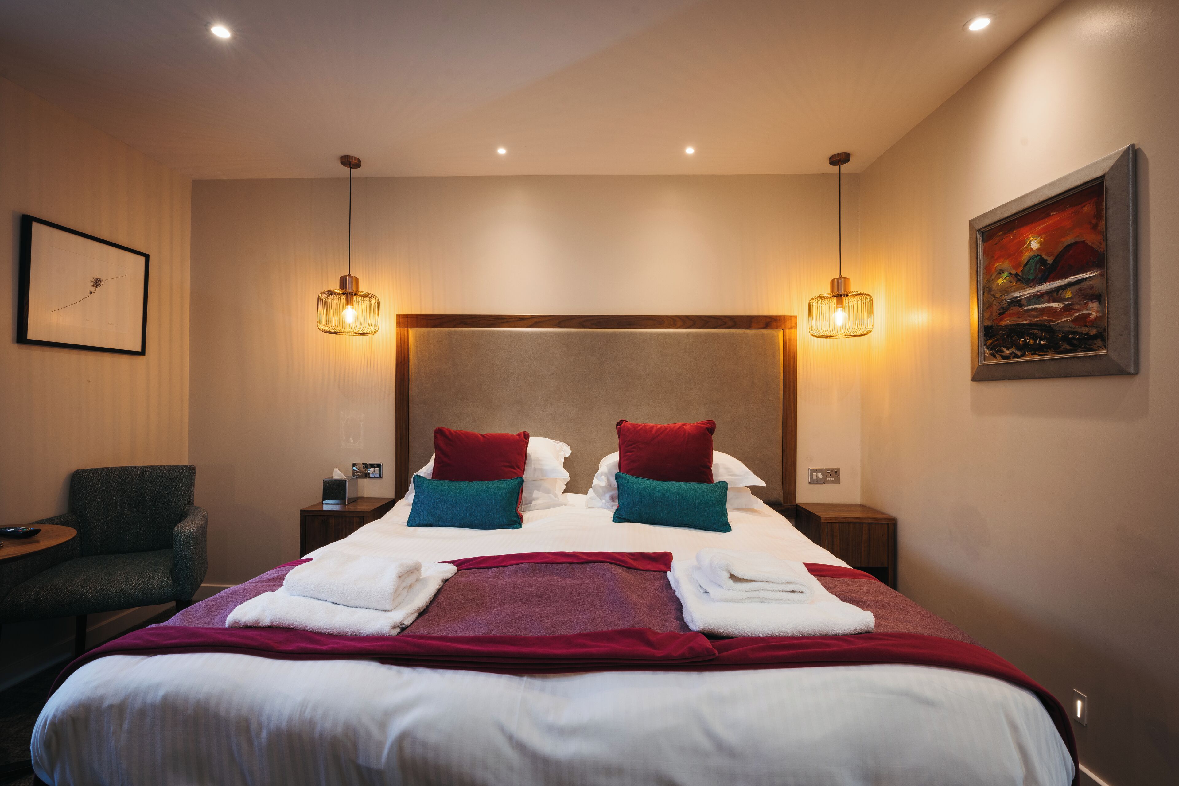 A hotel room with a large bed, two bedside tables, a chair, and a painting on the wall.