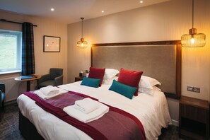 A hotel room with a large bed, two bedside tables, a chair, a small table, and a window with curtains. - Glaramara Hotel (Keswick)