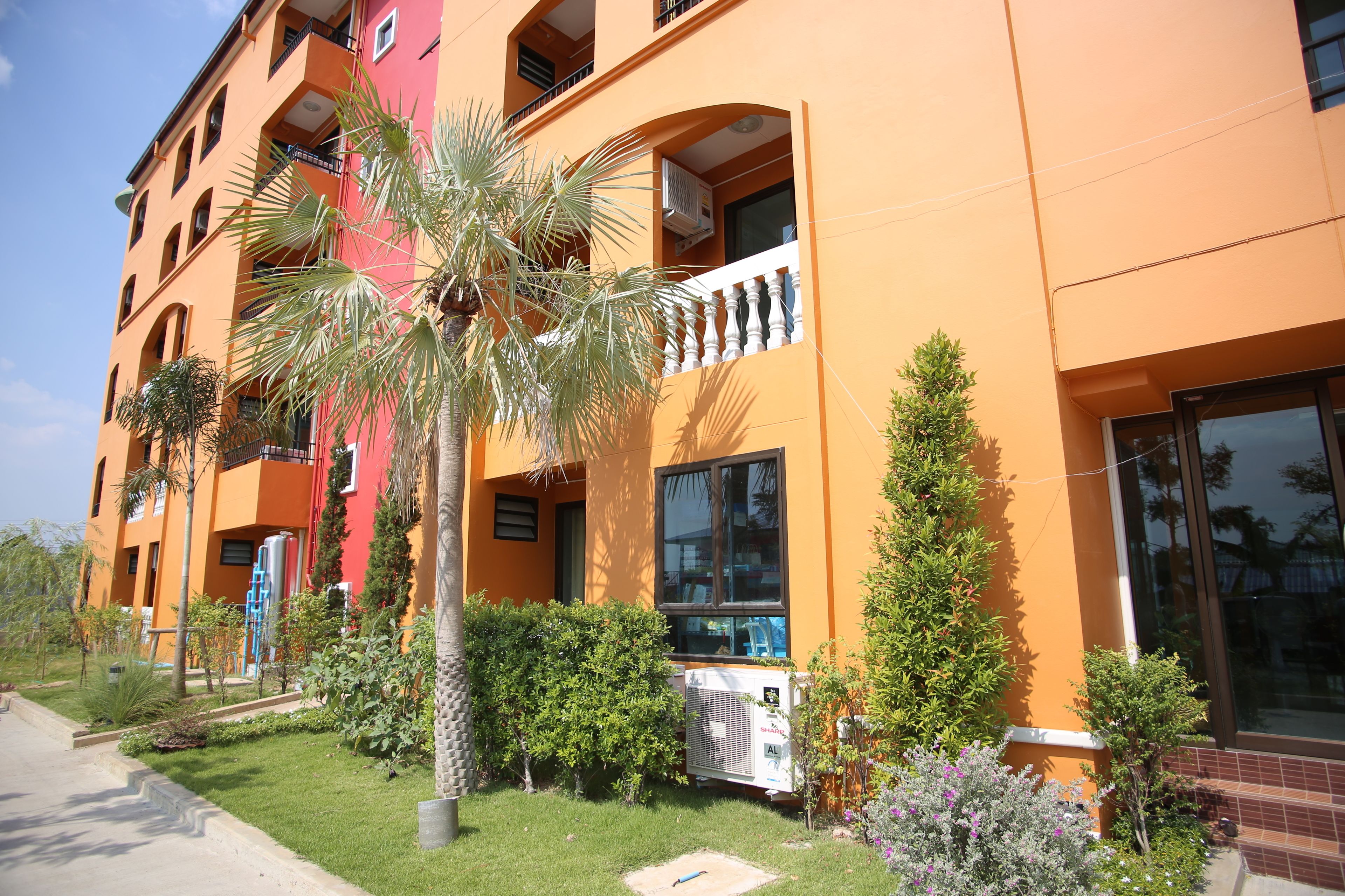 A multi-story building with balconies, air conditioning units, and a well-maintained garden with various plants.