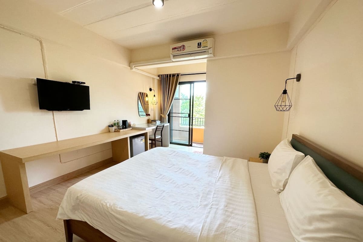 Una habitación de hotel con cama, escritorio, televisor y ventana con cortinas.