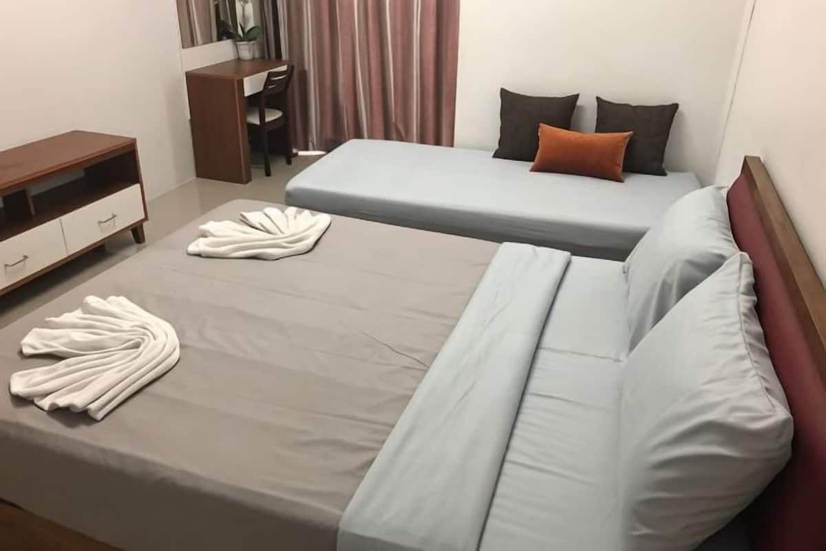 Un lit double avec un matelas gris, un bureau avec une chaise et un téléviseur.