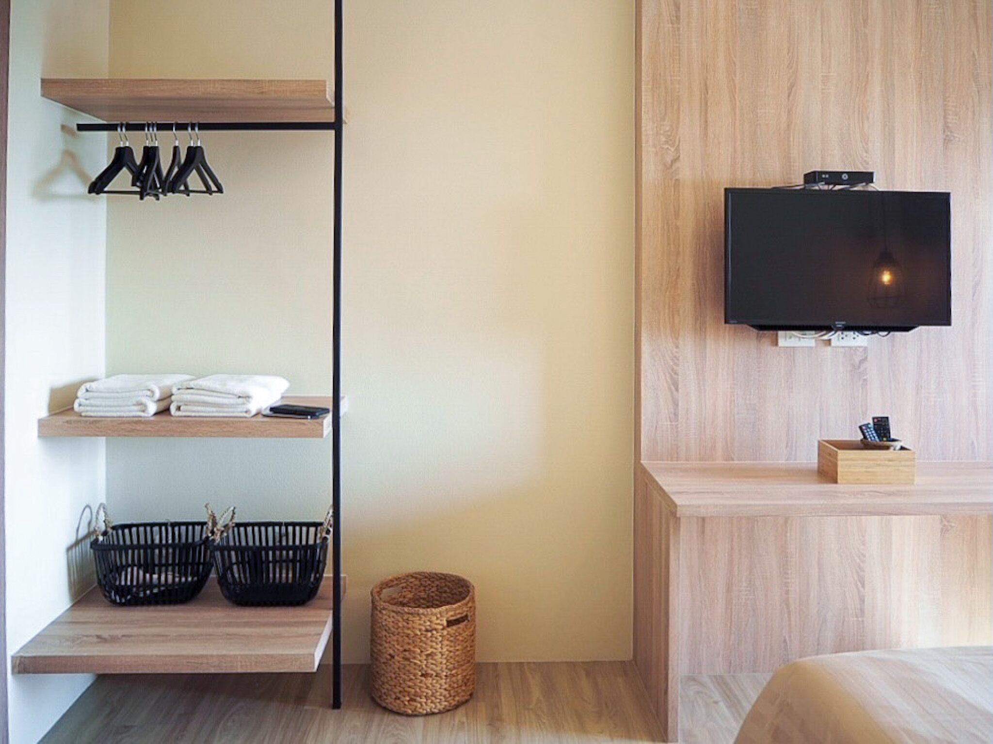 Habitación de hotel moderna con un mueble bajo de madera para el televisor, un televisor de pantalla plana, un estante con toallas dobladas y dos cestas.