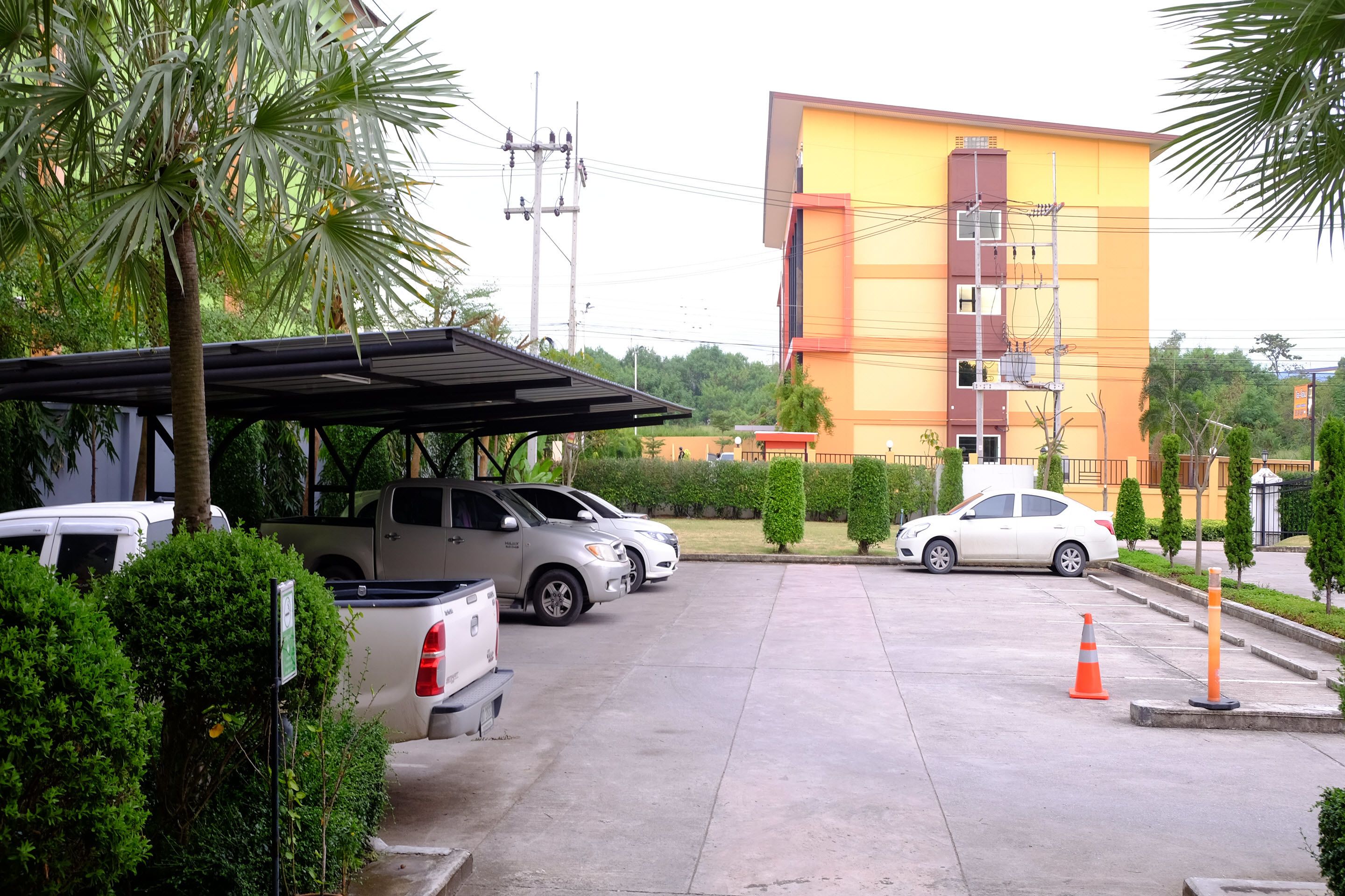 A parking area with several cars, a covered parking structure, and a multi-story building in the background.