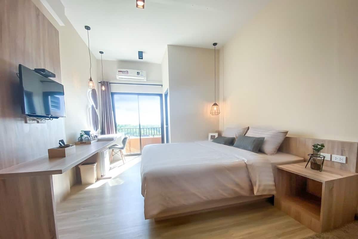 Una habitación de hotel moderna con una cama grande, un escritorio con una silla, un televisor montado en la pared y un balcón con vistas.