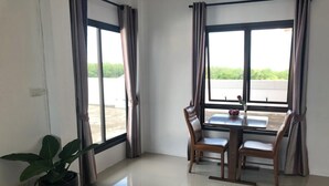 A room with a dining table and chairs, large windows with curtains, and a potted plant. - I-Home Residence and Hotel (Pluak Daeng)